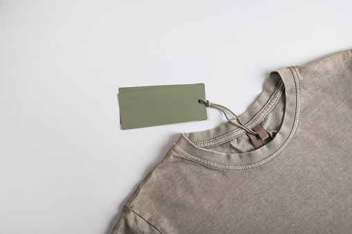 T-shirt with empty tag card or label mockup on pastel gray background. Top view, flat lay, copy space
