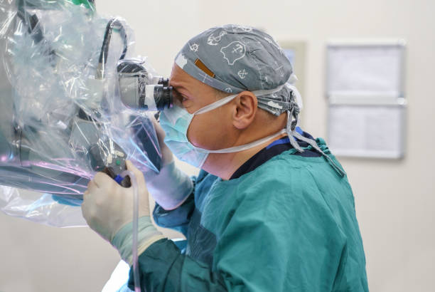 male neurosurgeon operating brain tumor surgery in hospital operating room. - robotchirurgie stockfoto's en -beelden