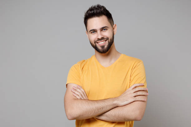 istock Young caucasian european bearded attractive handsome student man in casual yellow basic t-shirt hold hands crossed folded isolated on grey color background studio portrait People lifestyle concept. 1364765155