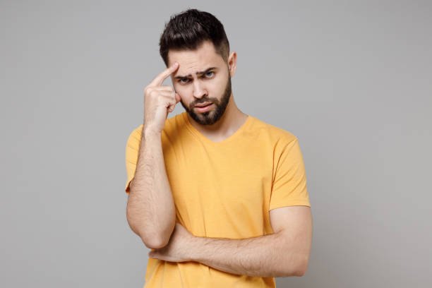 istock Young caucasian thoughtful pensive troubled bearded attractive sad student man 20s wearing casual yellow basic t-shirt prop up forehead head think isolated on grey color background studio portrait. 1364765751