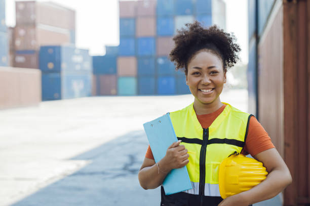 feliz trabajadora africana en la industria del transporte marítimo de carga portuaria de pie. - industrial ship dock worker engineer harbor fotografías e imágenes de stock