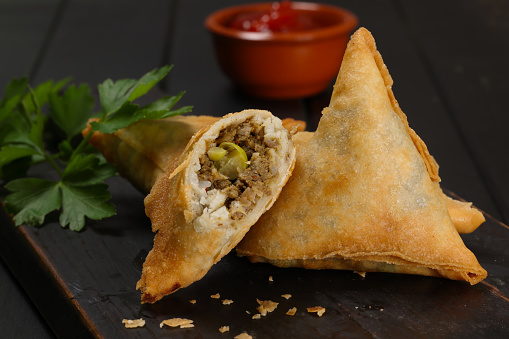 Samosa is a fried or baked pastry with a savoury filling, including spiced potatoes, onions, peas, chicken and/or other meats. It may take different forms, including triangular, cone, or half-moon shapes. High resolution image.