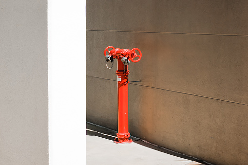 Bright red fire hydrant contrasts against a sand-coloured concrete wall and bright white wall in the foreground