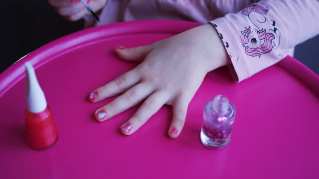 Curly little beautiful girl paints her nails with children's nail polish