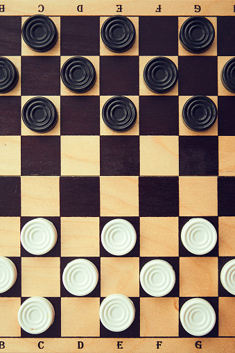 Checkers white and black on chess-board, top view, flat lay.