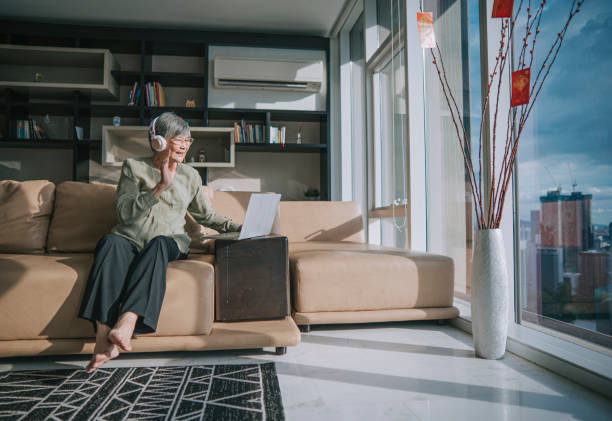 азиатский китаец пожилой женщины машет с помощью ноутбука видеоконференции с членами своей семьи во время китайского нового года в гостин� - malaysian person family asian ethnicity mother стоковые фото и изображения
