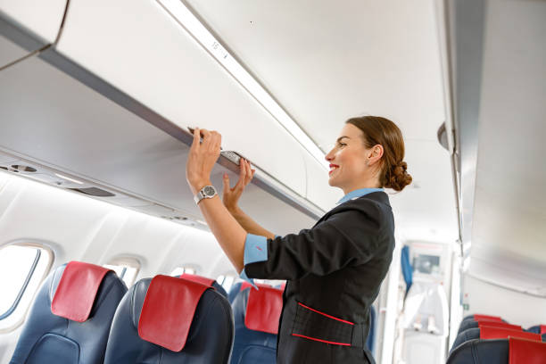 istock Joyful stewardess closing overhead luggage bin in airplane 1364780369
