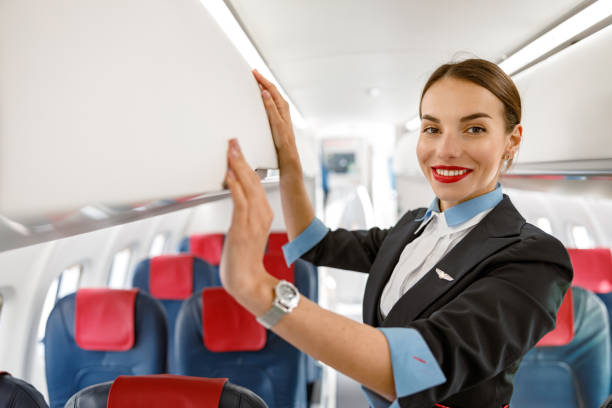 istock Cheerful stewardess standing by overhead luggage bin in aircraft 1364780372
