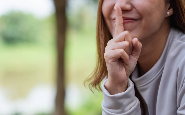 close-up de uma jovem asiática com dedo indicador nos lábios, pedindo para ficar quieto ou manter segredo - finger on lips whispering secrecy women - fotografias e filmes do acervo