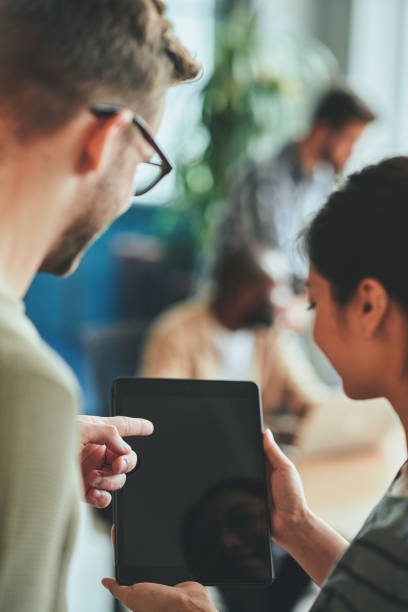 istock Two young people looking and pointing to blank tablet screen 1364780589