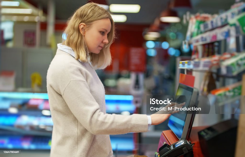 Woman pays at self-checkouts in supermarket. Kiosk Stock Photo