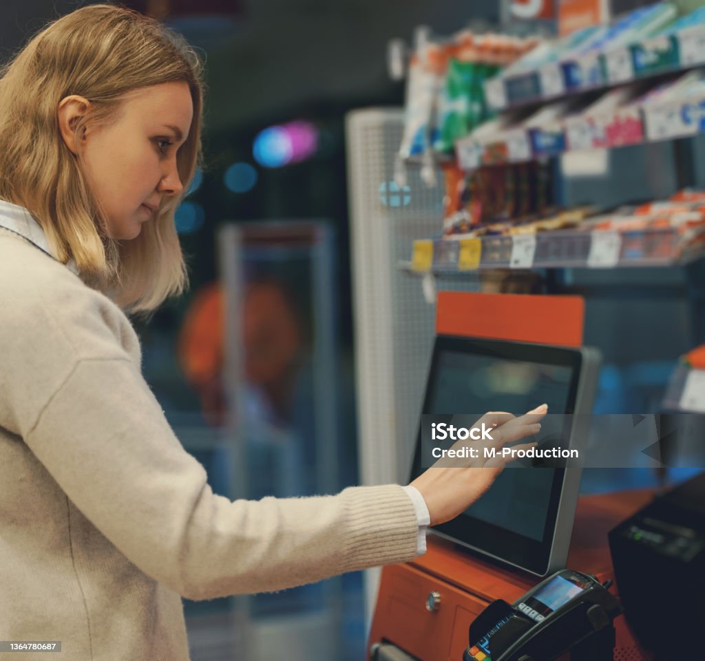 Woman pays at self-checkouts in supermarket. Kiosk Stock Photo