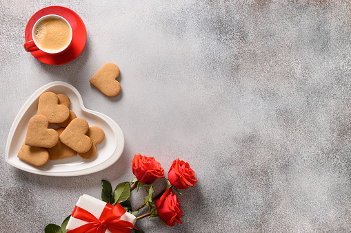 Valentine's day coffee and heart shaped cookies in plate, bouquet of red roses and love gift. View from above. Copy space.
