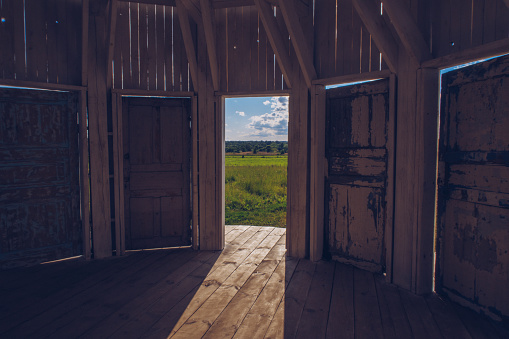 Inside white wooden Rotunda building with many doors with a view to a green meadow grass field