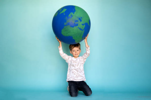 istock A little boy carrying globe while sitting on his knees against light blue background 1364798784