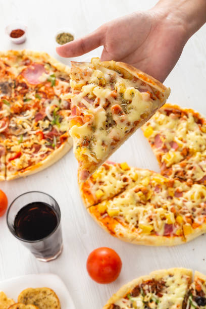 pizzas of different ingredients, glass with soda and a hand taking a piece, food and drink in studio, sharing and lifestyle - carbohydrate freshness food and drink studio shot imagens e fotografias de stock