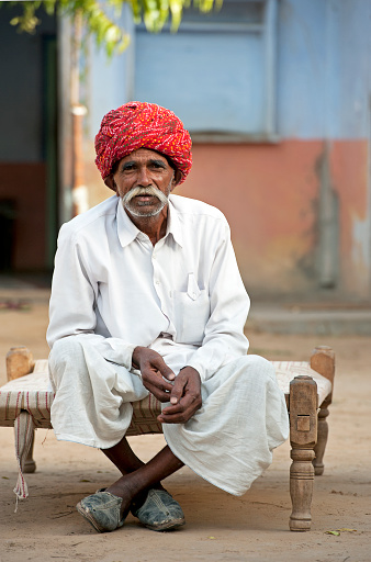 Seated man in red Pugaree, Samode, Rajasthan, India. The village of Samode in Rajasthan is a tranquil but busy town with a royal palace but more importantly is a remote rural collection of trades, stores and local people who have not been affected by tourism due to their location.