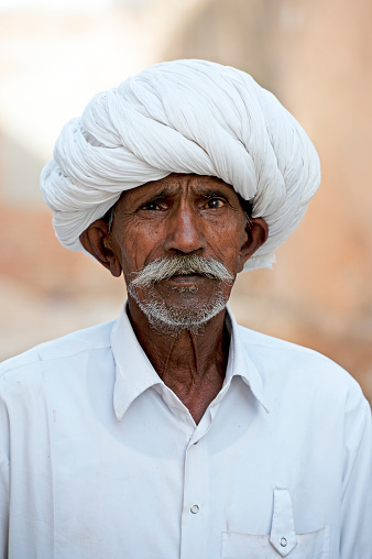 Senior man in white pugaree, Samode, Rajasthan, India. The village of Samode in Rajasthan is a tranquil but busy town with a royal palace but more importantly is a remote rural collection of trades, stores and local people who have not been affected by tourism due to their location.