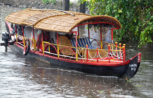 Keralan tourboat in the rain, Cochin, Kerala waterways, India. Kerala is a colourful Indian state of waterways and tropical rainforest geography on the southwestern Malabar Coast of the country owing its growth to the spice trade created by its Portuguese and British colonial occupiers that is now an attraction for tourists with its river boats and canals