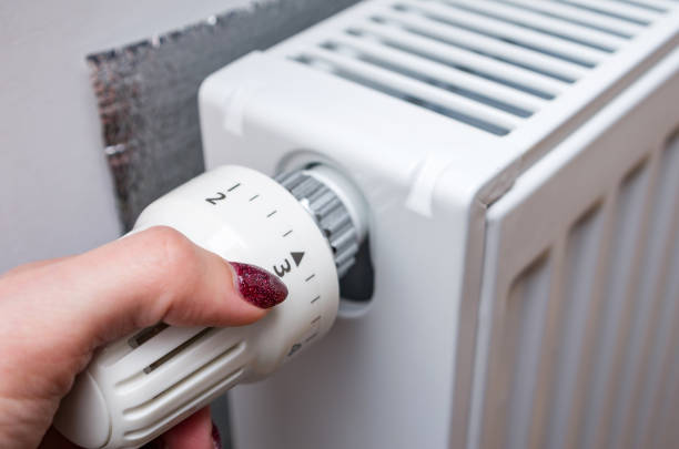 Woman's hand turning a heating thermostat. stock photo