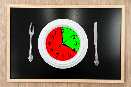 Clock with one portion marked in red and another in green. Concept of intermittent fasting, a diet that provides benefits such as the regenerative mechanism of autophagy.