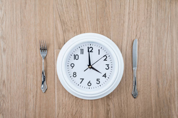 istock Clock with a knife and fork on a wooden background. 1364812967