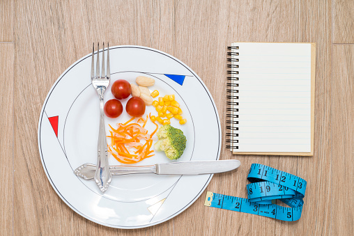 Dish with cutlery, healthy food, tape measure and a notebook on a wooden background. Conceptual image of intermittent fasting, a diet with benefits such as the regenerative mechanism of autophagy.