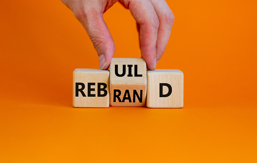 Rebrand and rebuild symbol. Businessman turnsa the wooden cube and changes the word rebrand to rebuild. Beautiful orange table, orange background. Business rebrand and rebuild concept. Copy space.