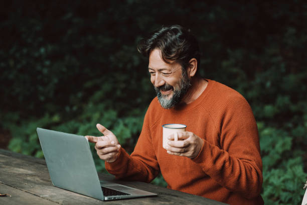 Adult hipster bearded man enjoying video call conference outdoors in the nature using laptop computer. Concept of modern people and digital nomad smart working job activity outdoors stock photo