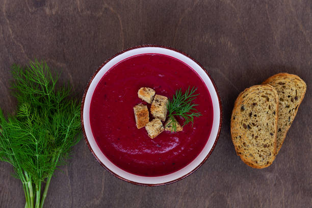 beet soup with bread and herbs.Bowl of Beetroot cream soup with white cream and croutons on a brown wooden background. Healthy dietary lunch. Flat lay, top view. copy space