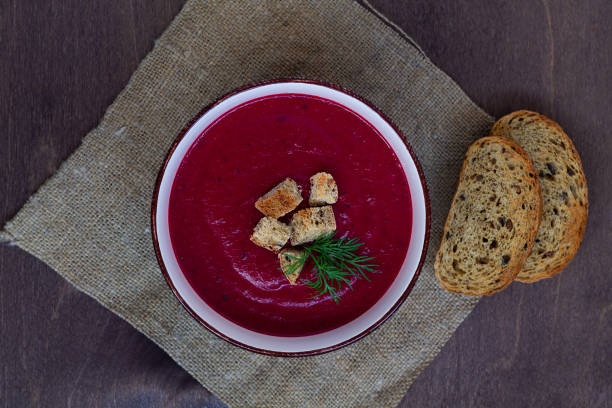 vegetable soup with greens and bread on the sackcloth. Bowl of Beetroot cream soup with white cream and croutons on a brown wooden background. Healthy dietary lunch. Flat lay, top view. copy space