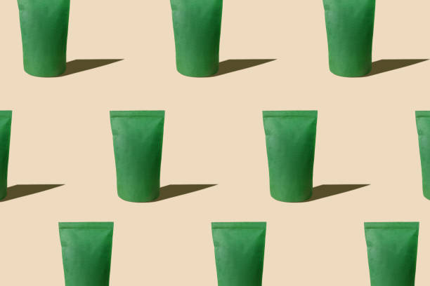 istock Green pouch bag mockup pattern neutral beige background harsh shadows. Blank emerald recycled paper pack coffee beans. 1364822628
