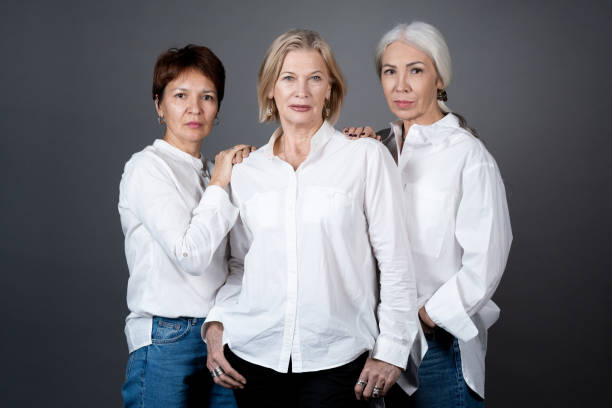 Beautiful mature women posing Portrait of beautiful mature women in white shirts posing at camera against the grey background middle aged woman fashion stock pictures, royalty-free photos & images