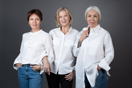 Portrait of stylish mature women posing at camera together against the grey background