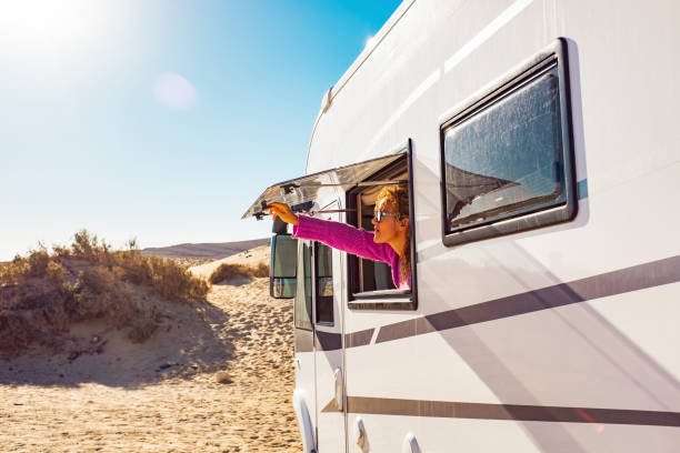 Adult tourist woman opening camper van window to enjoy the sun and freedom. Concept of travel people for summer holiday vacation inside camping car motorhome vehicle. Freedom nomad lifestyle stock photo