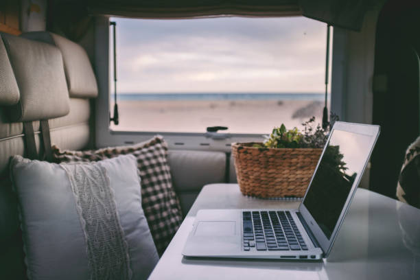 Remote onilne work and smart working travel concept with laptop computer inside a van camper interior with beach view. Freedom from office modern lifestyle for alternative life and people
