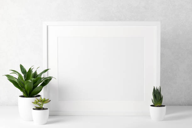 istock Frame mockup with white wooden frame on a white table, houseplants. Show text or product. 1364826781