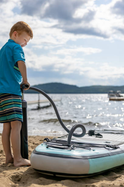 istock Cute Redhead Boy Inflating Paddleboard SUP at the Beach in Summer, Quebec 1364827674