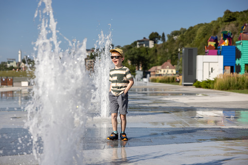 Cute Redhead Boy Playing in the Water Fountain, Fontaine du Quai Paquet, Lévis, Quebec, Canada. He is playing in the water with his clothes on and will all be wet.