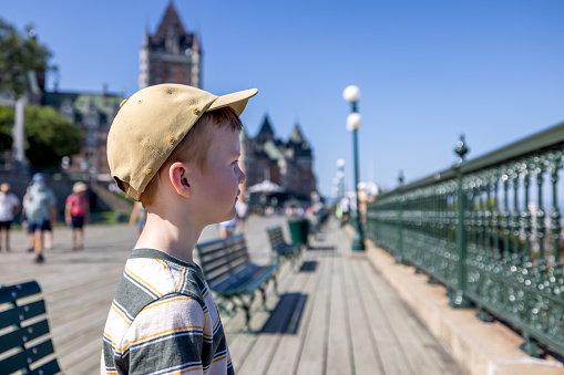 Cute Redhead Boy Sitting on Bench at Chateau Frontenac Hotel in Quebec City, Canada. The bench is location on the boardwalk in front of the castle.