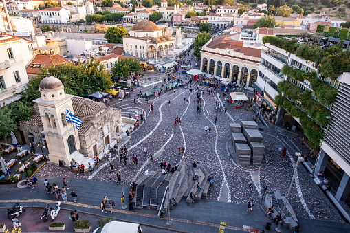 Aerial view of Monastiraki Square, the flea market neighborhood in the old town of Athens. Photo contains many locals and tourists visiting the square. The clustered homes on the hill is known as Plaka.