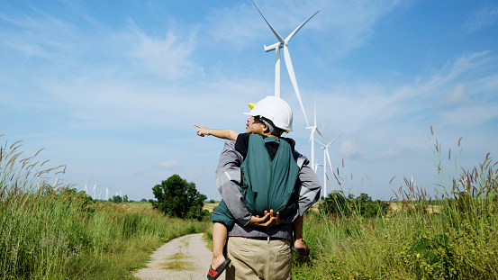 engineer father and his son playing Piggyback in a wind turbine field, father teaching his son how to live in harmony with nature and technology, family relationships.