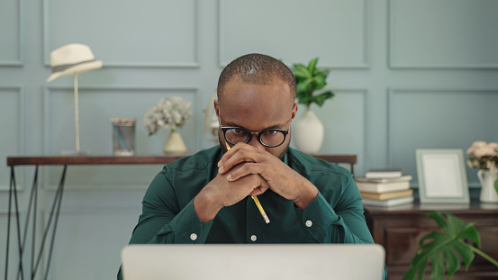 young african American man is thinking in front of a laptop.