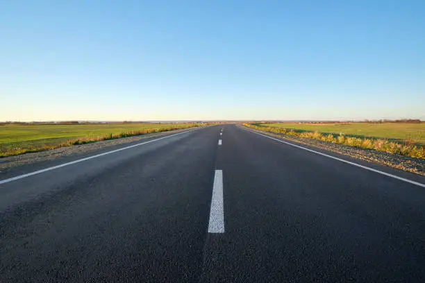 Empty intercity road with asphalt surface and white markings in evening.