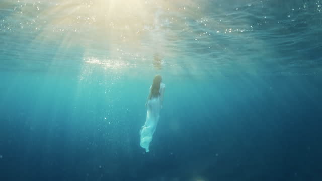 SLO MO Woman in white dress swims underwater