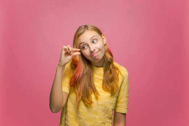 Photo of Cute young girl look at hand showing with fingers something small with pity, little size gesture on pink background