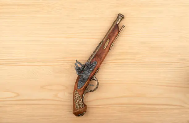 Antique single-shot muzzle-loading pistol with a percussion lock on a wooden background. Close up.