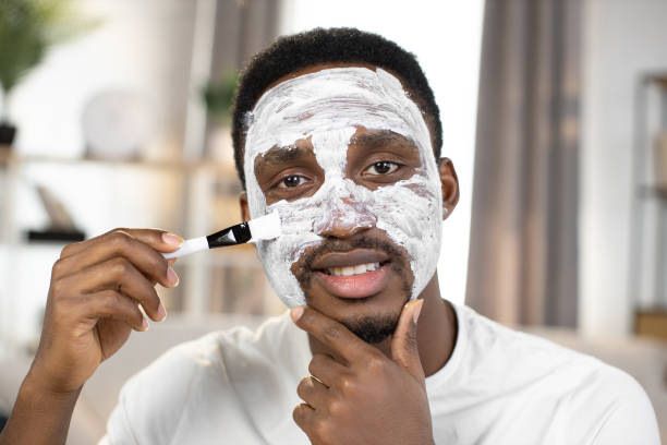 istock handsome african american applying white clay mask on his face with brush 1364838166