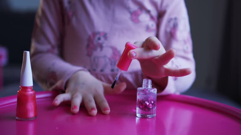 Curly little beautiful girl paints her nails with children's nail polish