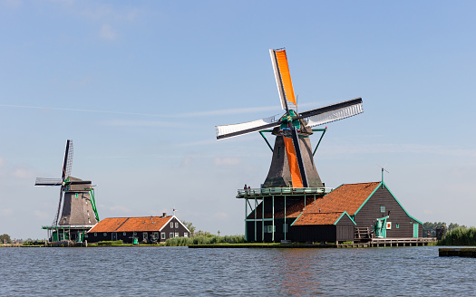 Close-up of two of the historic windmills at the Zaanse Schans in North Holland, seen from the Zaam river on a sunny summer day - the Zaanse Schans is one of the most popular tourist attractions of the Netherlands, in 2017 it had a total of 2,2 million vistors